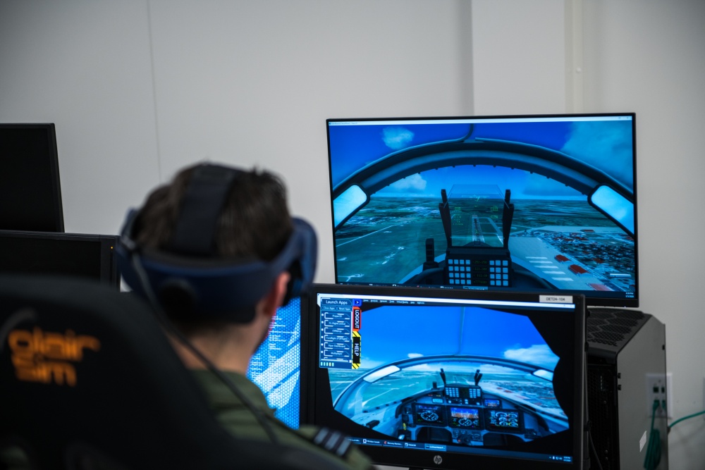 Image shows aviator using virtual reality headset and looking at screen display of a cockpit.